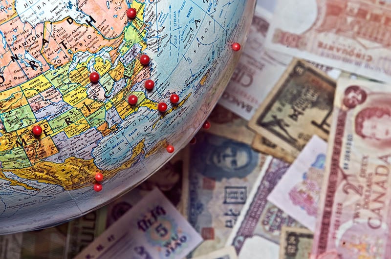 globe with pins sitting on money of different currencies
