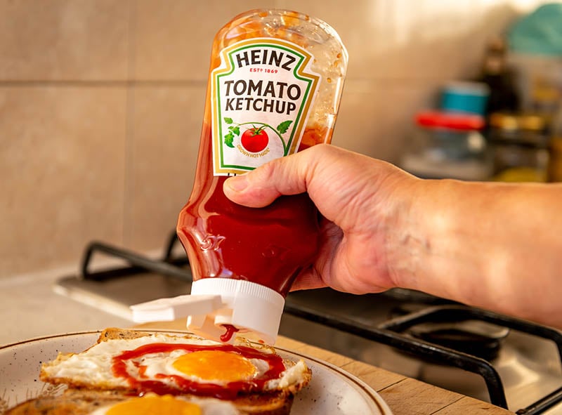 tomato ketchup being squeezed onto a fried egg